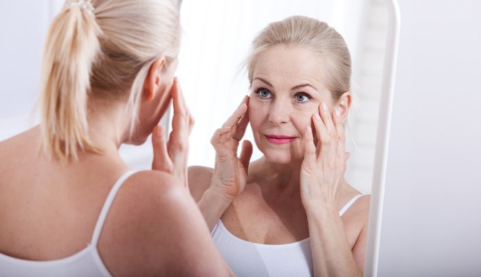 item 1 of Gallery image A woman looking at her face in a mirror