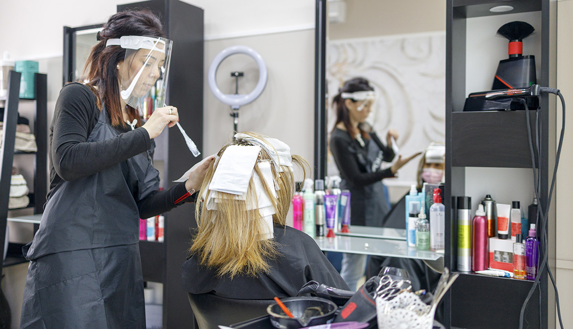 item 8 of Gallery image - A hair dresser applying highlights to a customer sitting in a chair in front of a mirror