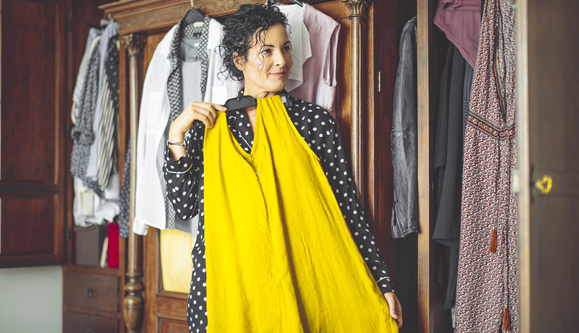 item 7 of Gallery image - A woman is examining a yellow dress with her body in front of a mirror