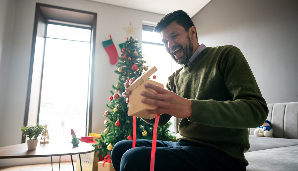 A smiling man opens a holiday gift inside his home