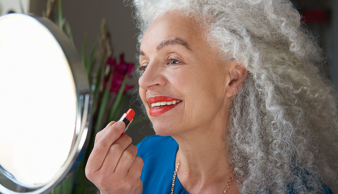 Una mujer aplicando un lápiz labial color rojo mientras se mira al espejo.