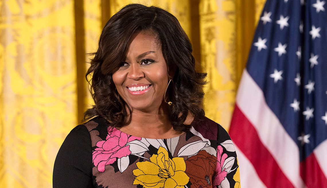 Michelle Obama sonriendo y al fondo una cortina amarilla y la bandera de Estados Unidos