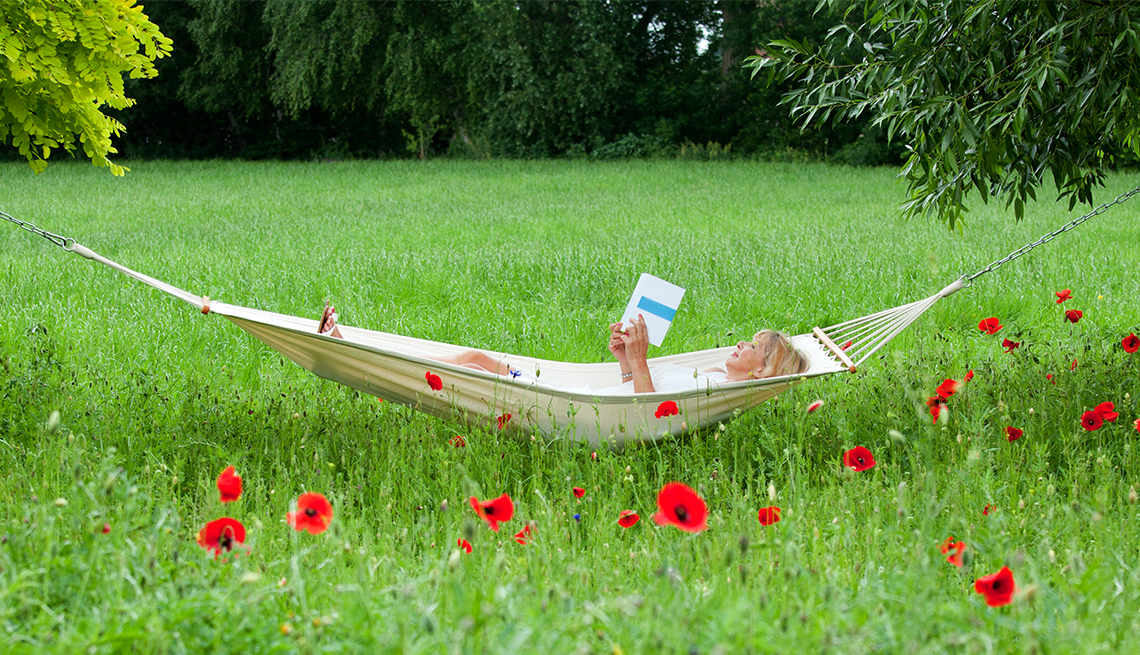 Mature woman lying on hammock in garden reading book.
