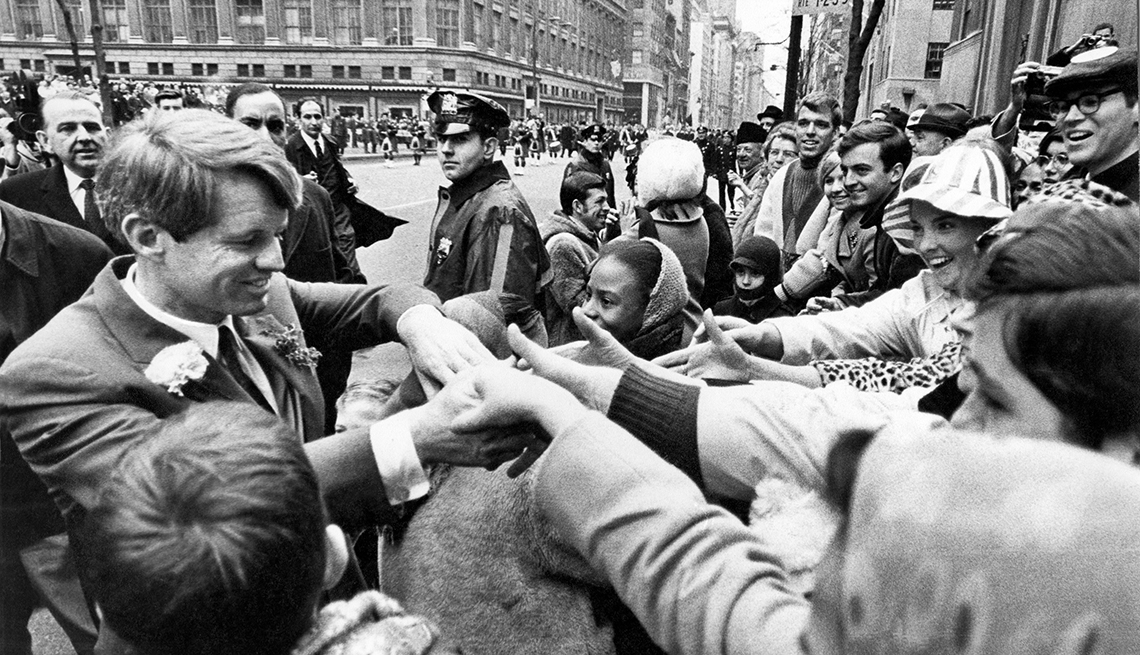 Robert F. Kennedy in the middle of a crowd shaking hands.