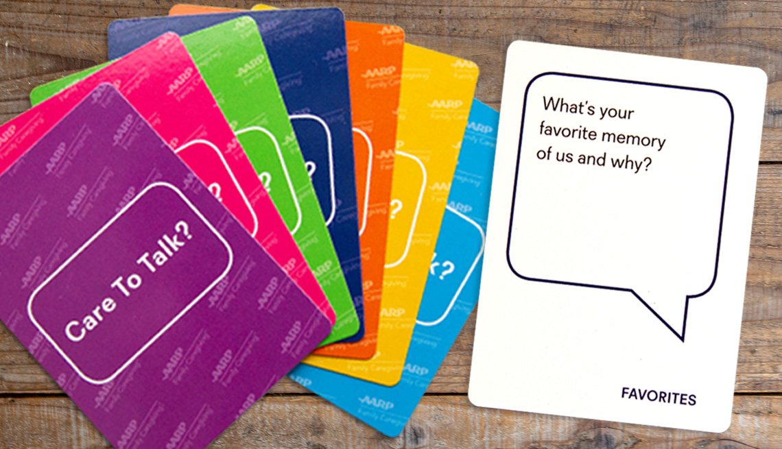 product photo of the family card deck on a wooden table. shown are a fan of seven different colored card backs that read care to talk, and a sample question card that asks, what is your favorite memory of us and why
