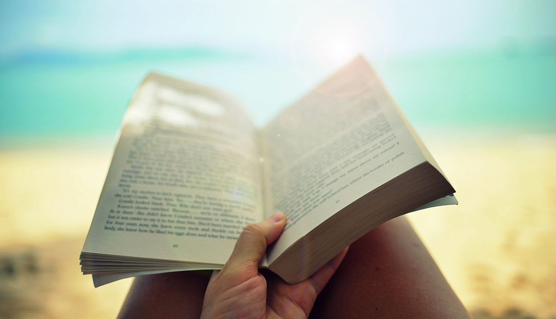 womans view looking down at a book in her lap on a sunny beach