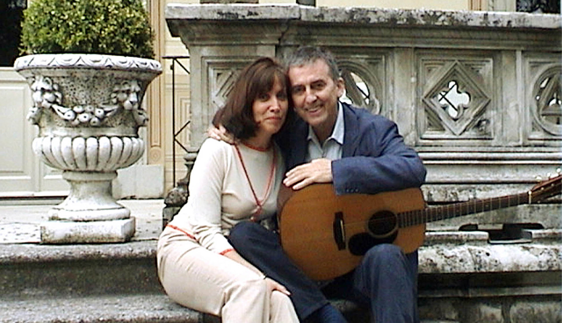 George Harrison sitting with an acoustic guitar alongside his wife Olivia posing for a photo while on vacation in Italy