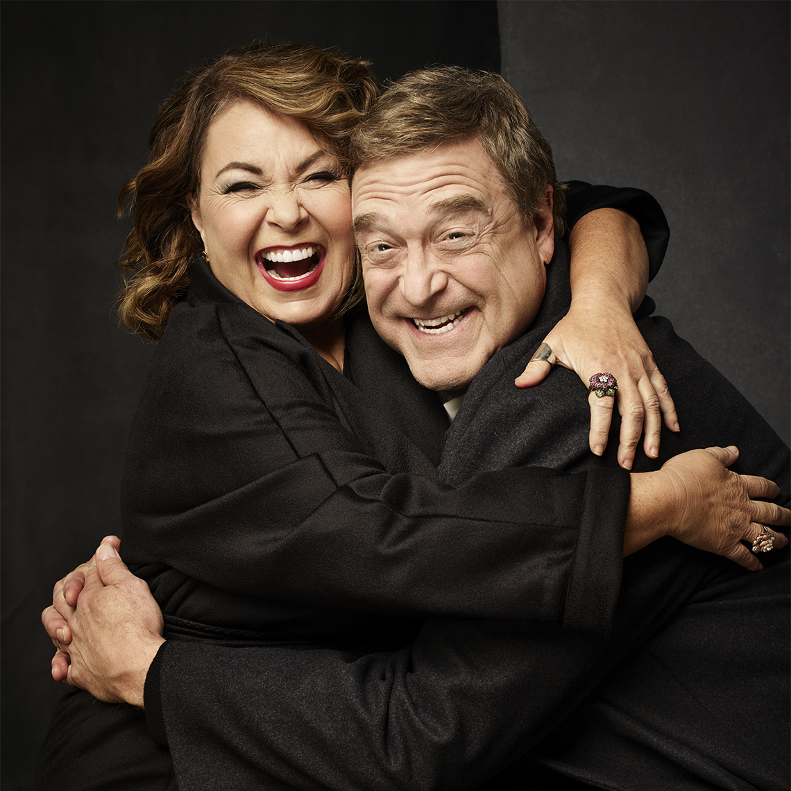 Roseanne Barr and John Goodman laughing and hugging each other