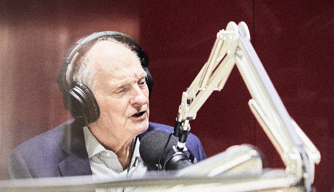 actor alan alda hosting a podcast talking into a microphone in a sound booth