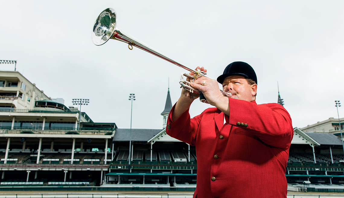 A man in red coat and black hat blowing a bugle at Churchill Downs