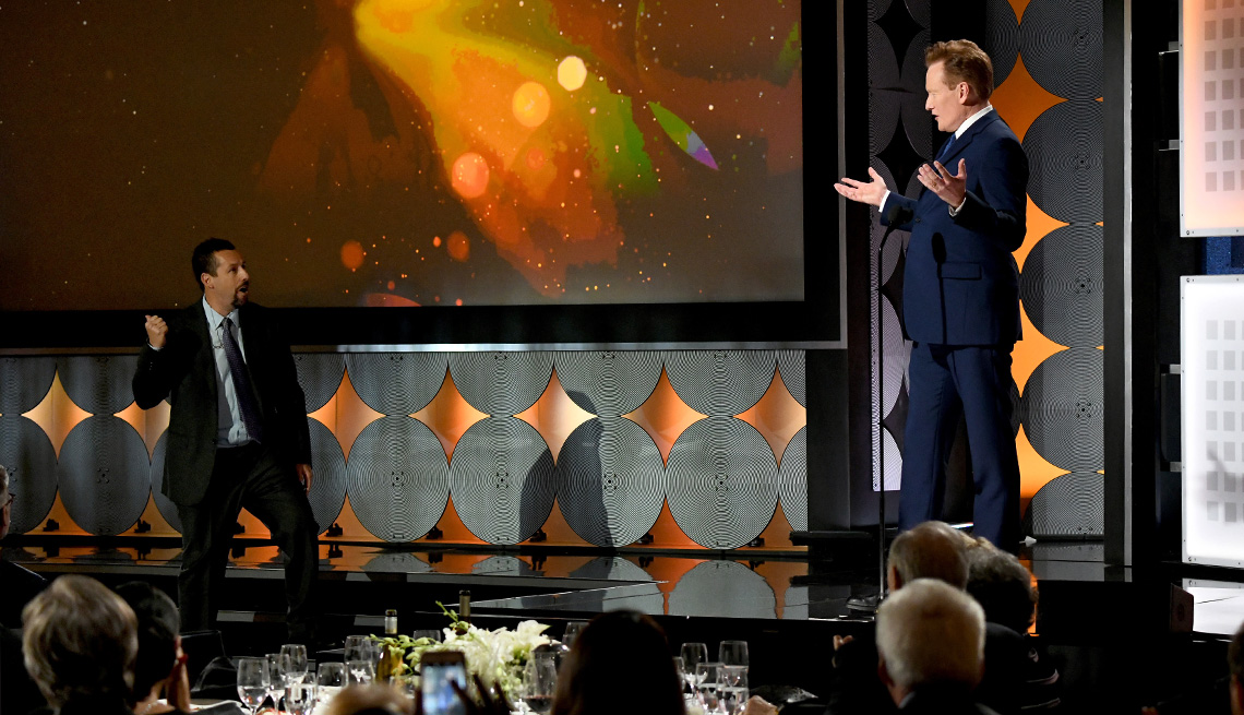 Conan O Brien raises his hands as Adam Sandler comes to the stage too early during the presentation of the Best actor award at the Movies for Grownups Awards