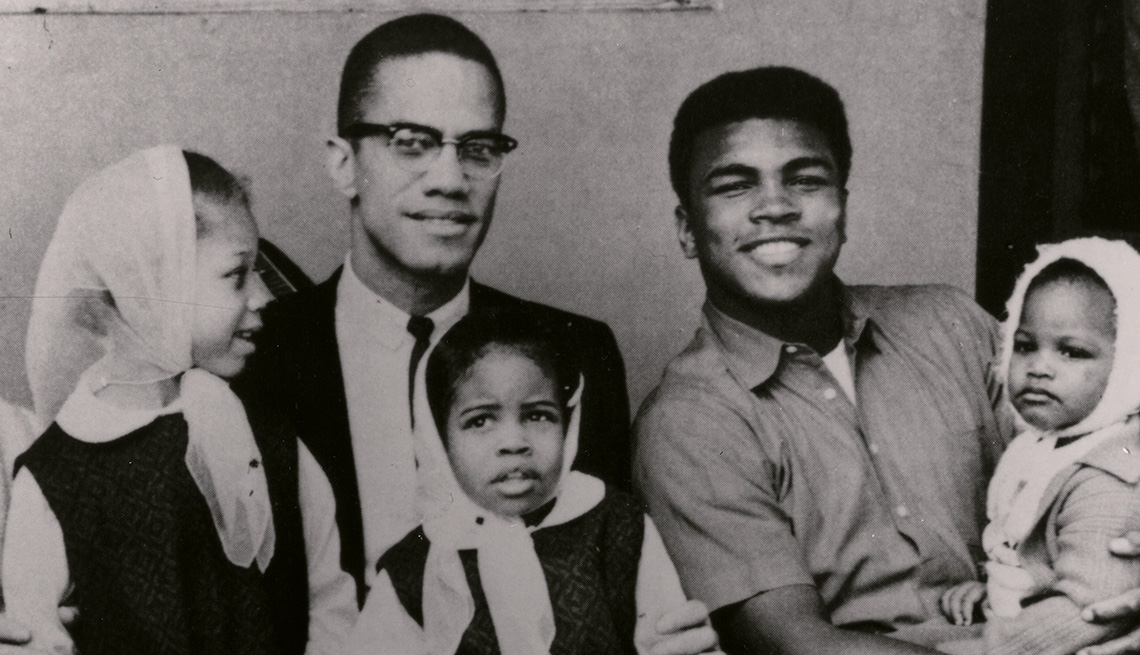 Malcolm X y Muhammad Ali sentados uno al lado del otro mientras sostienen a sus hijas en sus regazos.