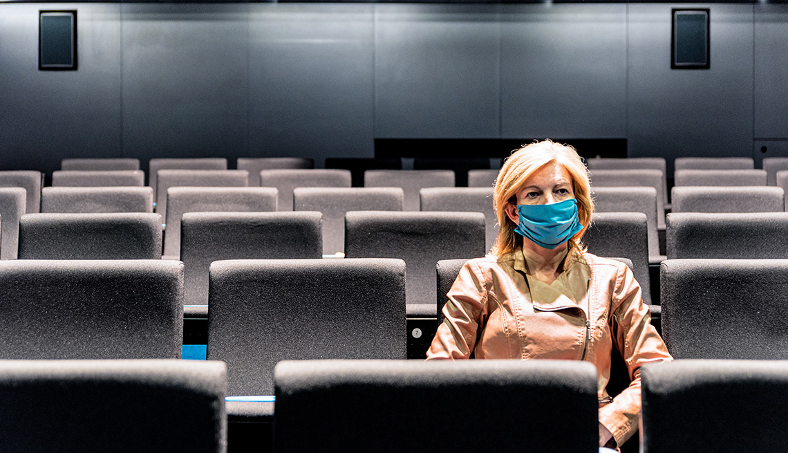 A woman wearing a protective face mask sitting in an empty movie theater
