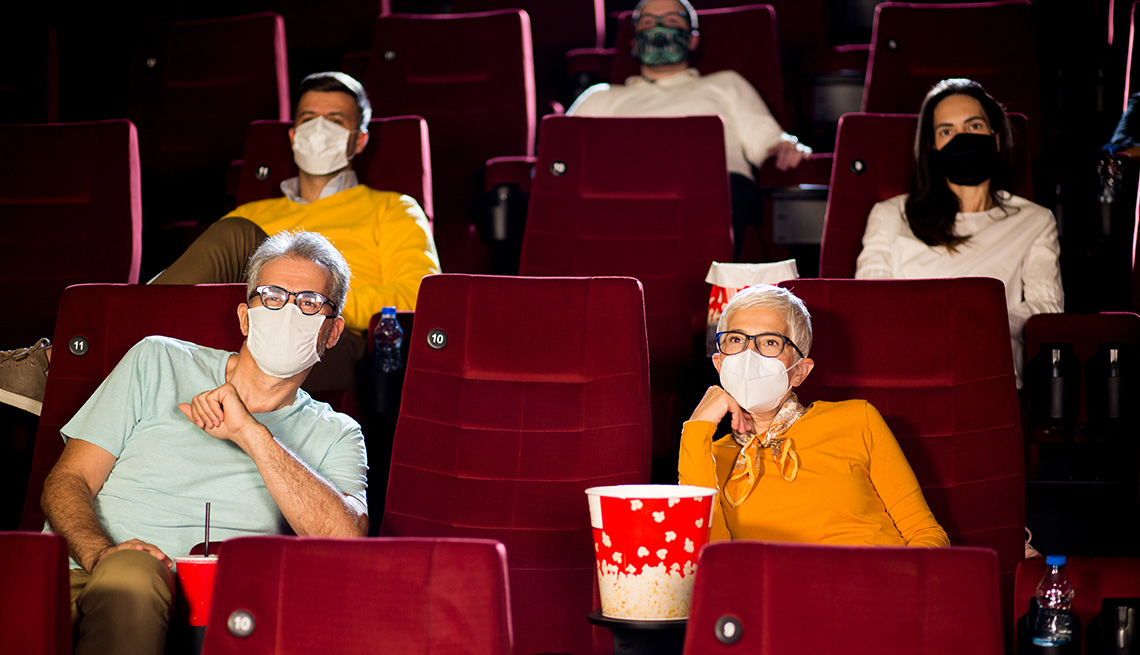 Público en el cine con máscaras protectoras y sentado a distancia mientras ve una película.