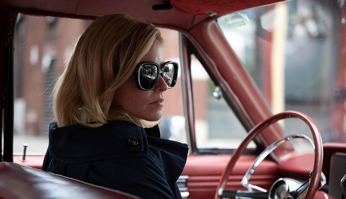 Elizabeth Banks wearing sunglasses while sitting in the drivers seat of a car in the film Call Jane