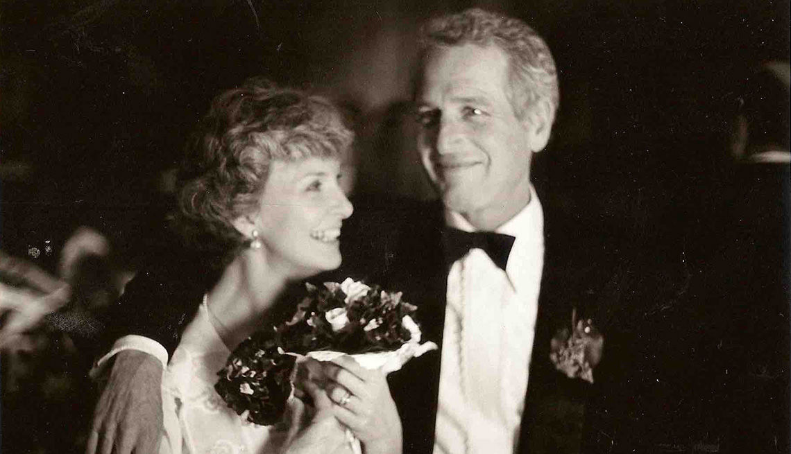 Joanne Woodward sosteniendo flores junto a su esposo Paul Newman vistiendo un esmoquin.