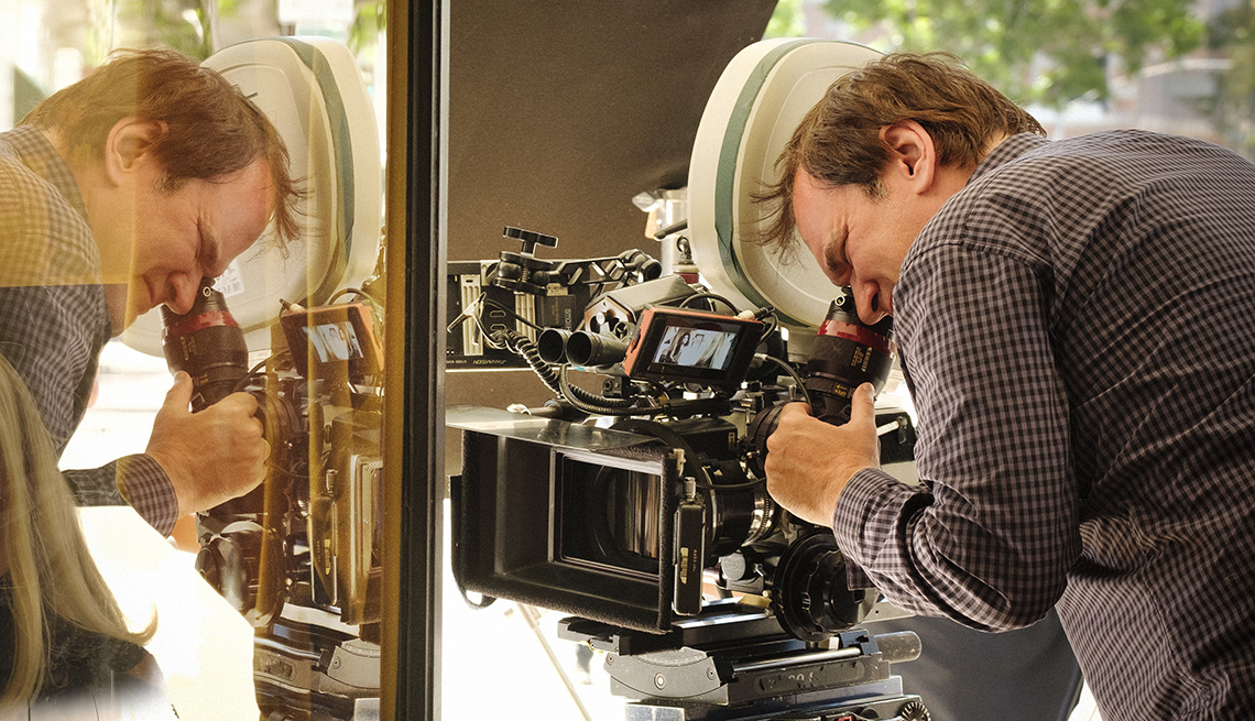 Director Quentin Tarantino looking into a camera lens while directing a scene from the film Once Upon a Time in Hollywood