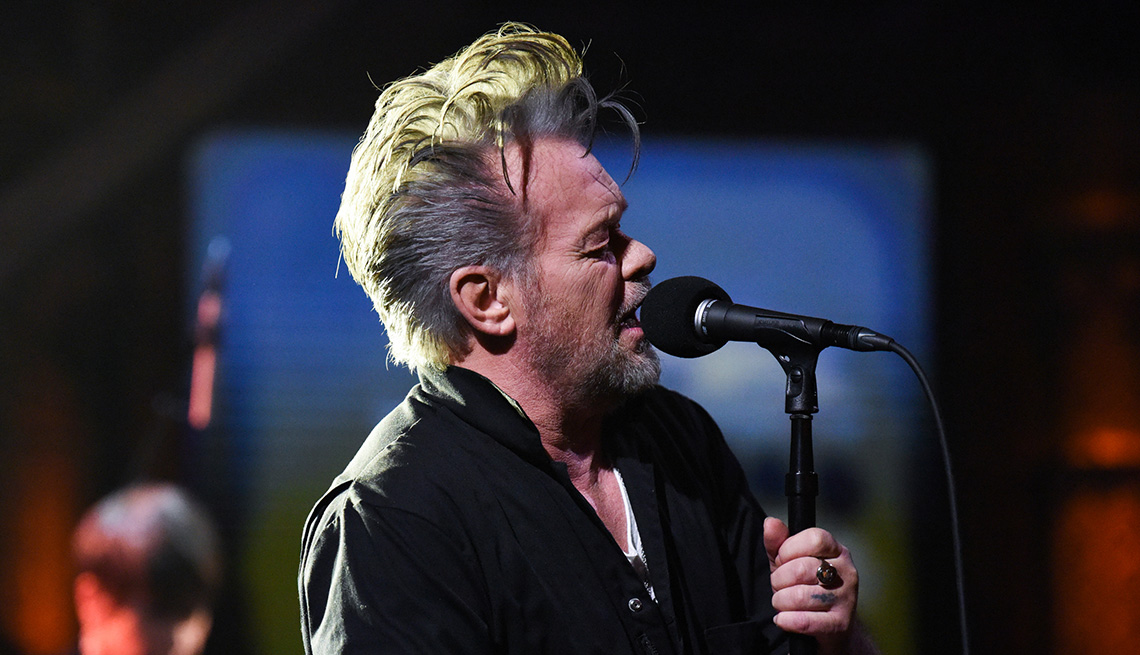 John Mellencamp holding a microphone on stage.