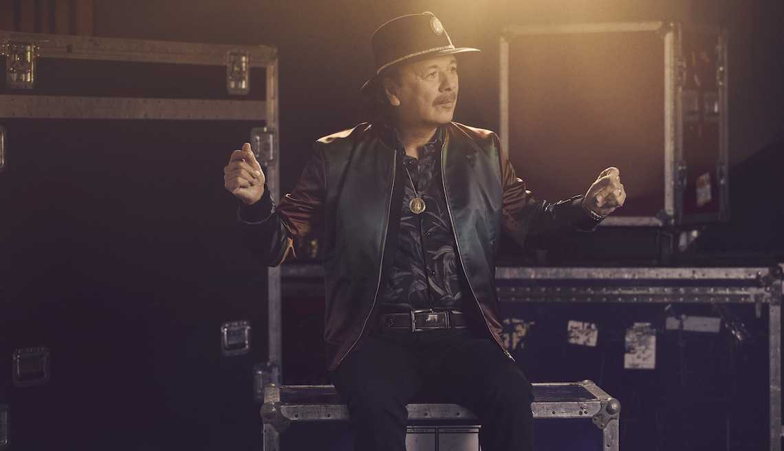 Carlos Santana snapping his fingers while sitting on music equipment crates