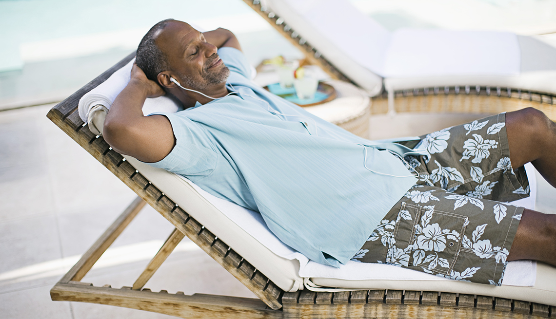 A man lying on a pool chair relaxing while wearing headphones listening to music