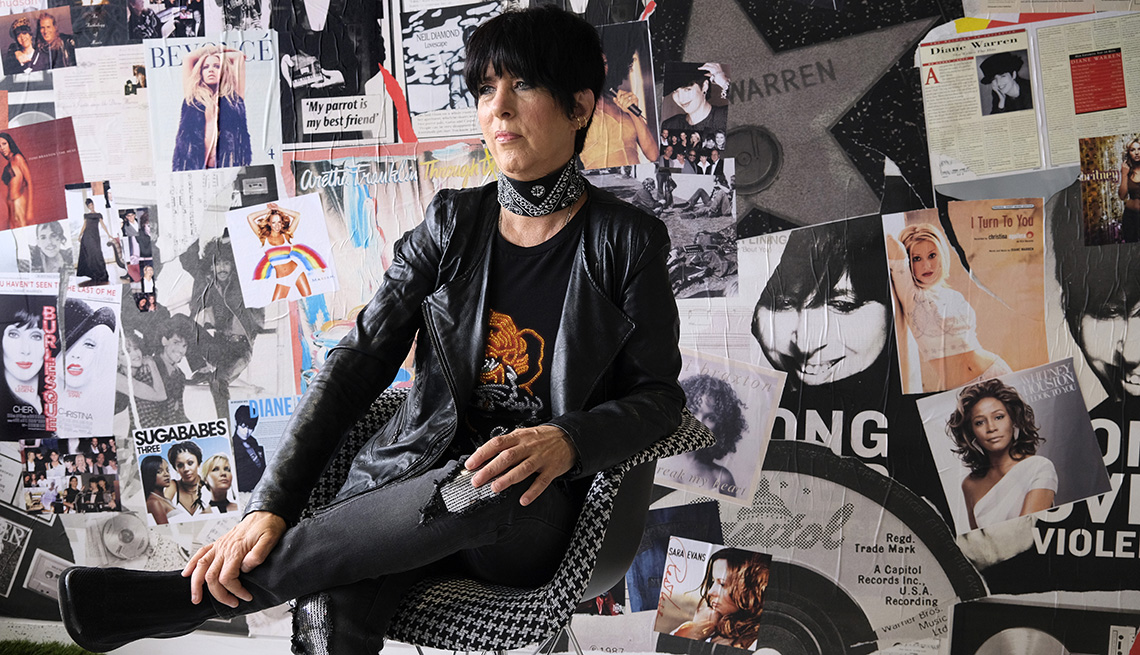 La compositora Diane Warren se sienta en una silla en su oficina y posa para un retrato frente a una pared llena de portadas de revistas y álbumes.