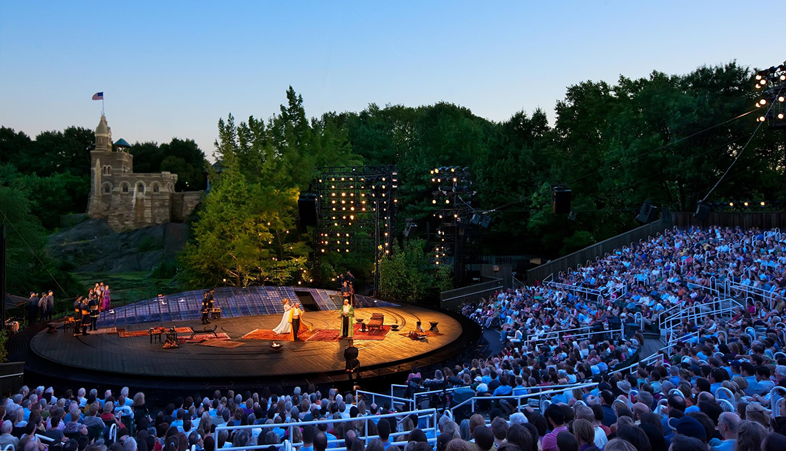 A performance happening at the Delacorte Theater's stage with a full crowd watching