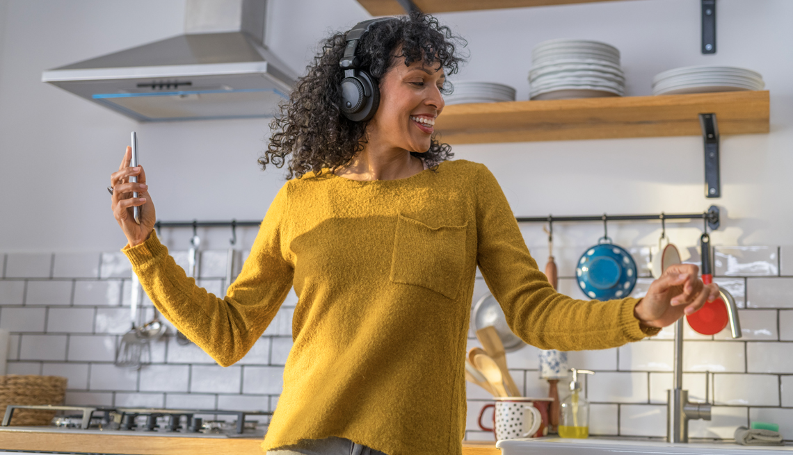 woman dancing in her kitchen wearing headphones and holding a smart phone