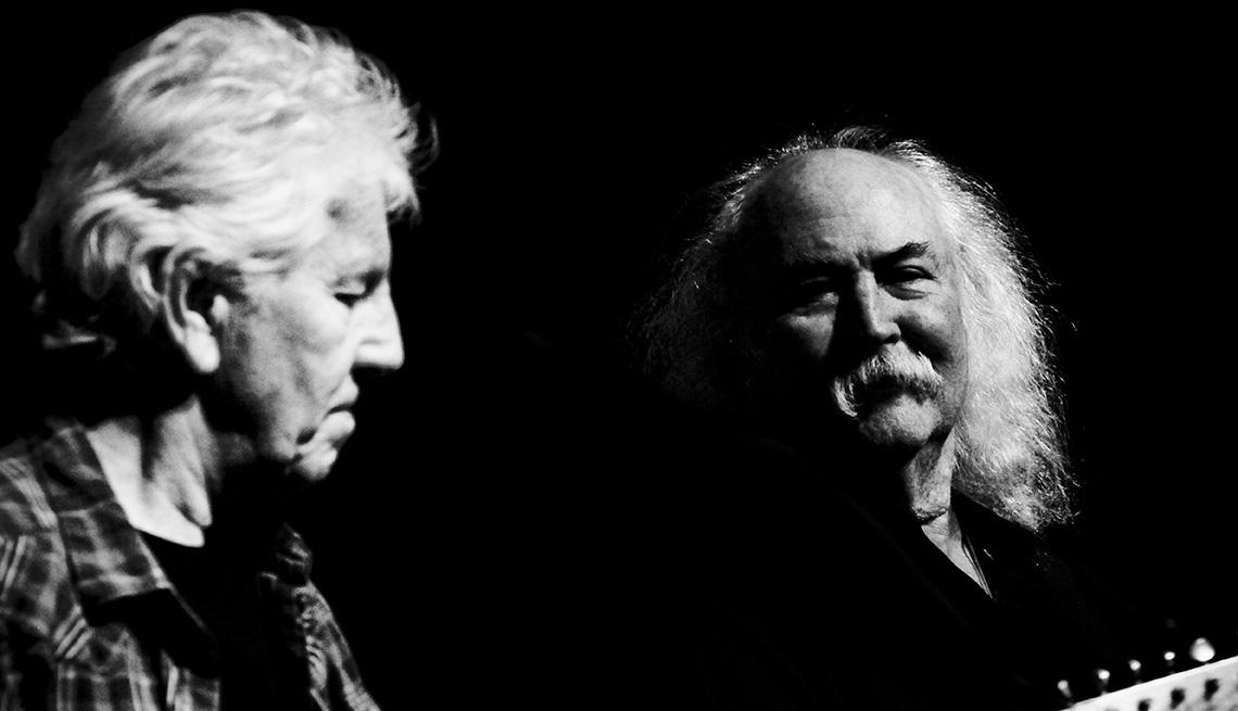 Graham Nash playing the guitar as David Crosby look on next to him