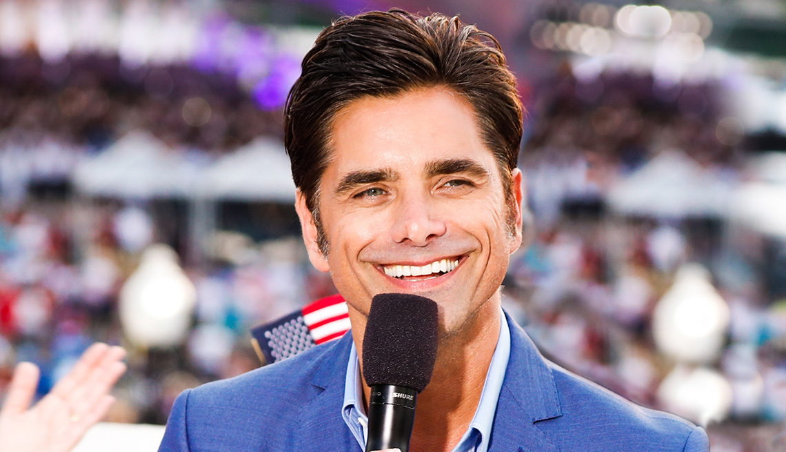 Close up of John Stamos holding a microphone. 
