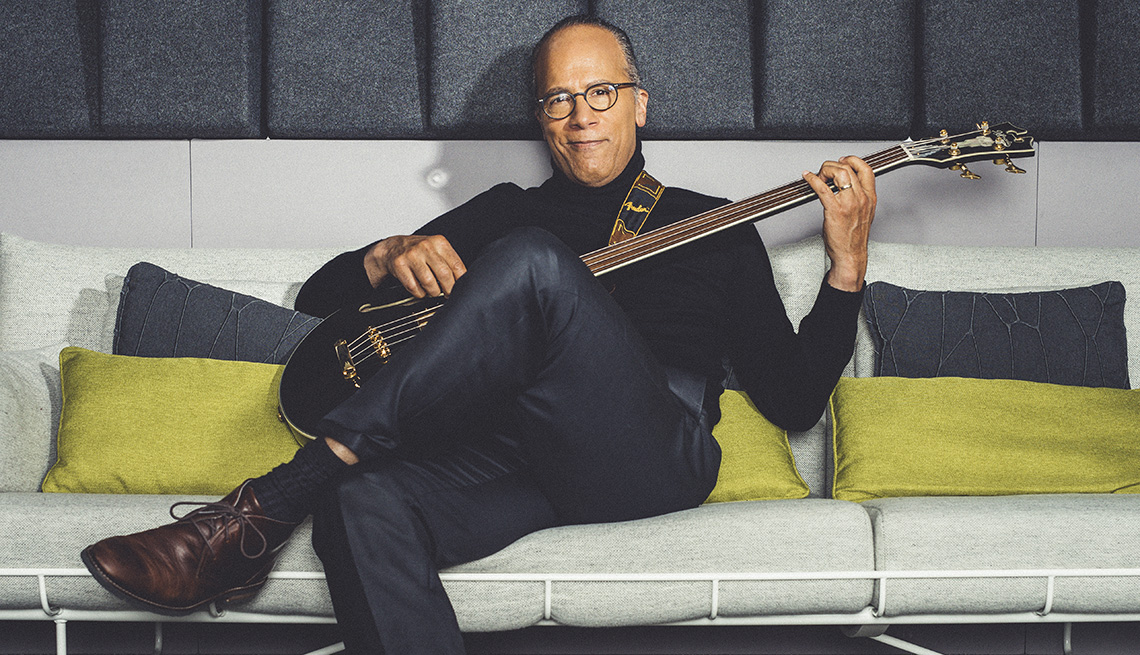 Lester Holt sitting on a couch holding a bass.