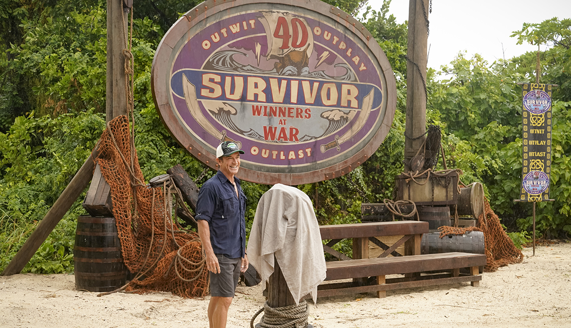 Jeff Probst in front of a sign on a beach as he hosts Survivor Winners at War the 40th season of the television reality series
