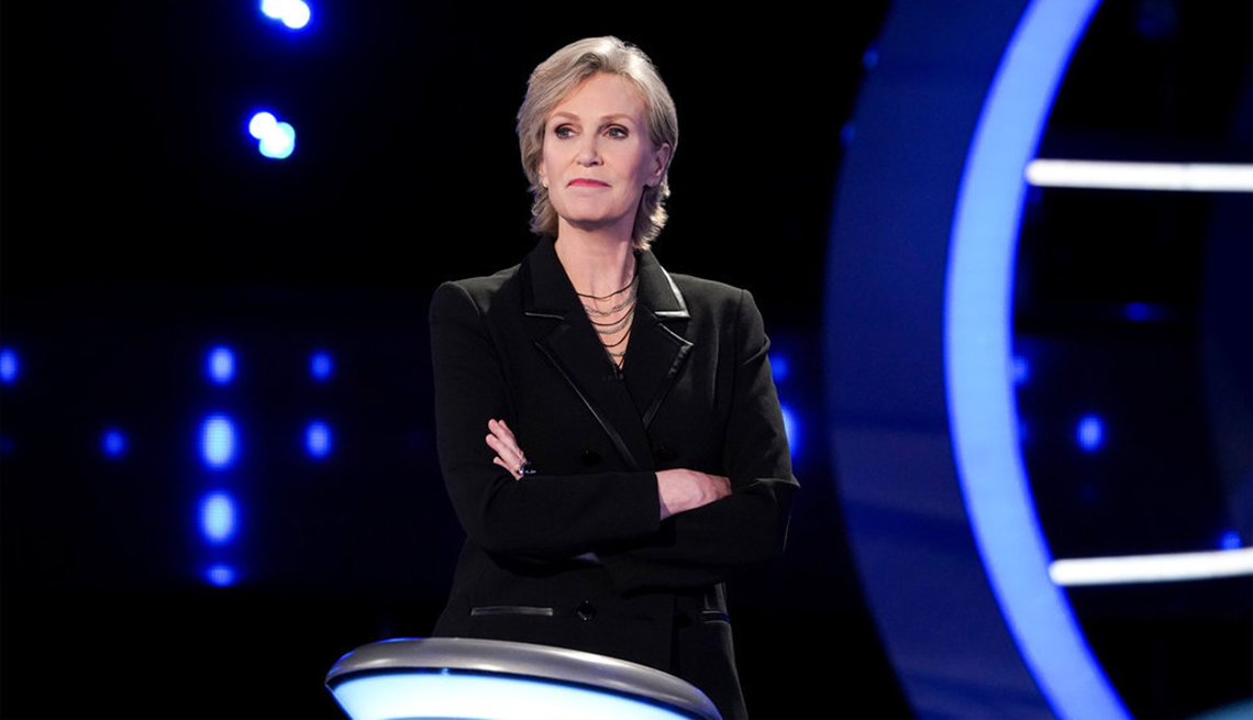 Jane Lynch stands at the podium as the host of the NBC show Weakest Link