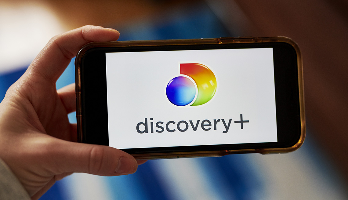 Una persona que sostiene un teléfono inteligente con el logotipo del servicio de transmisión Discovery Plus.