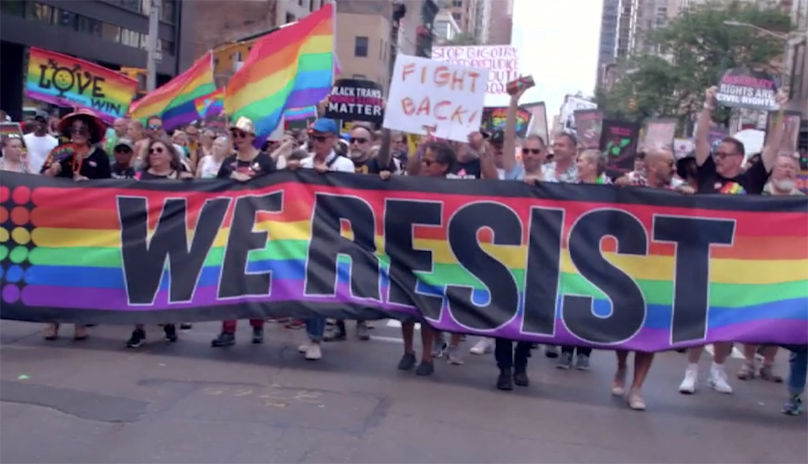 A crowd at an LGBTQ rally holding a sign that says "We Resist"