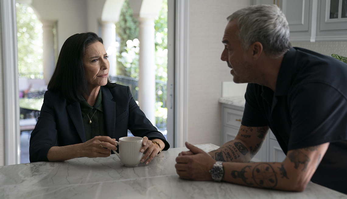 Mimi Rogers sitting at a kitchen counter while touching a coffee cup with her hands while talking to Titus Welliver in a scene from Bosch Legacy