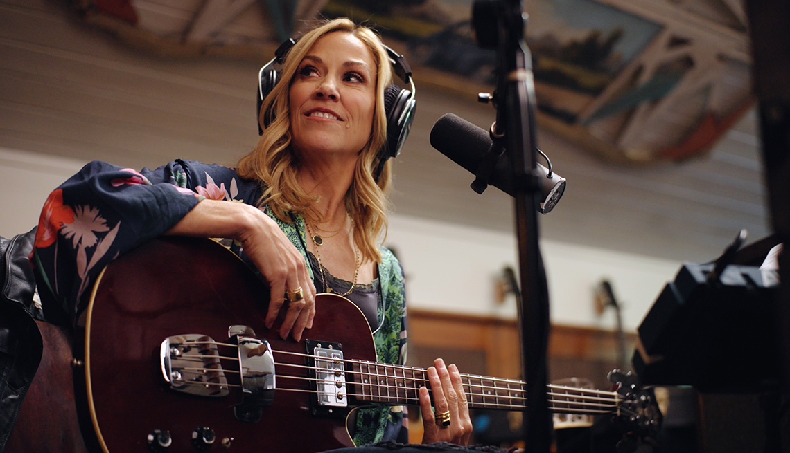 Sheryl Crow with her guitar wearing headphones and sitting behind a microphone in a scene from the Showtime documentary Sheryl