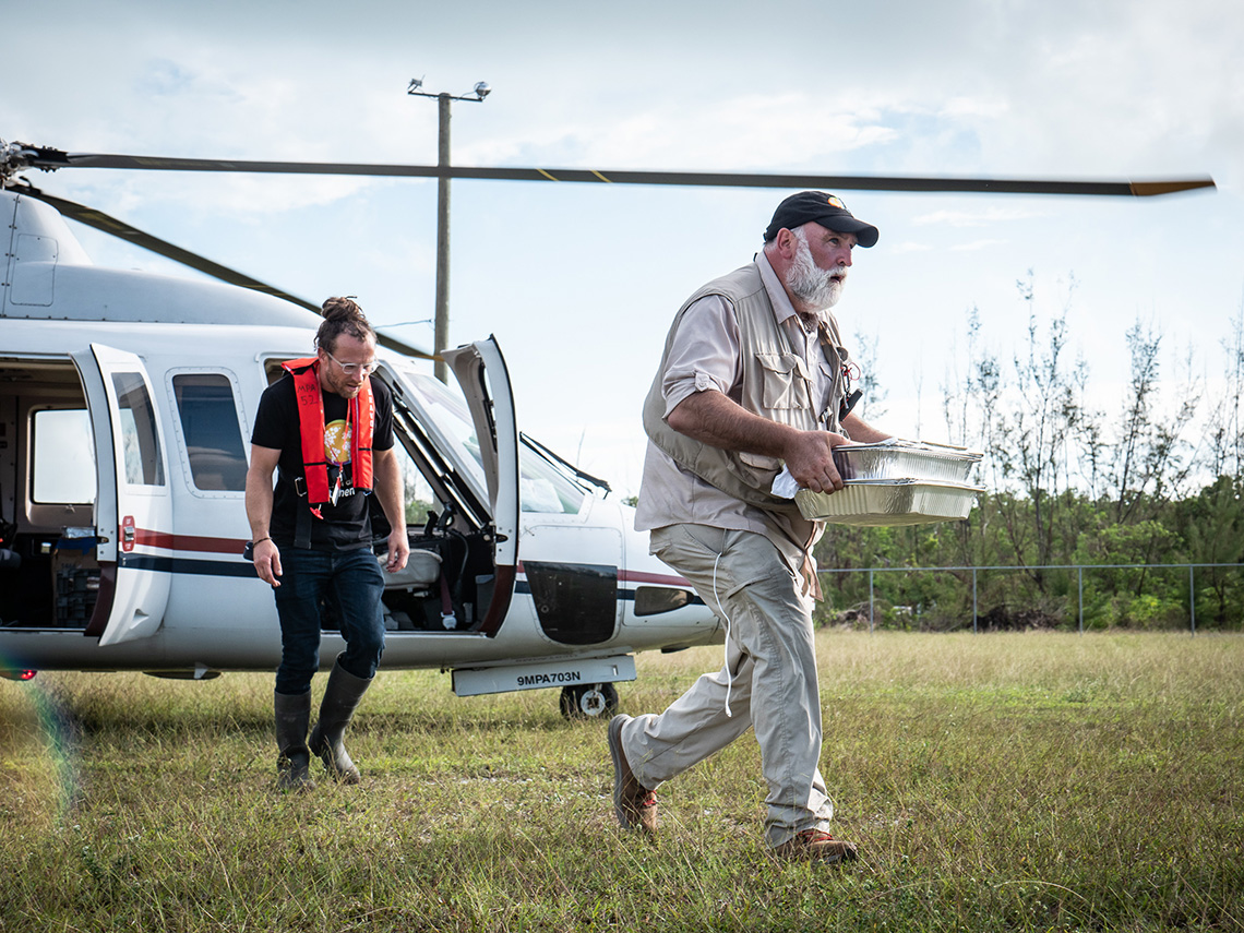Chef José Andrés carrying a tray of food from a helicopter with World Central Kitchen's director of emergency response Sam Bloch