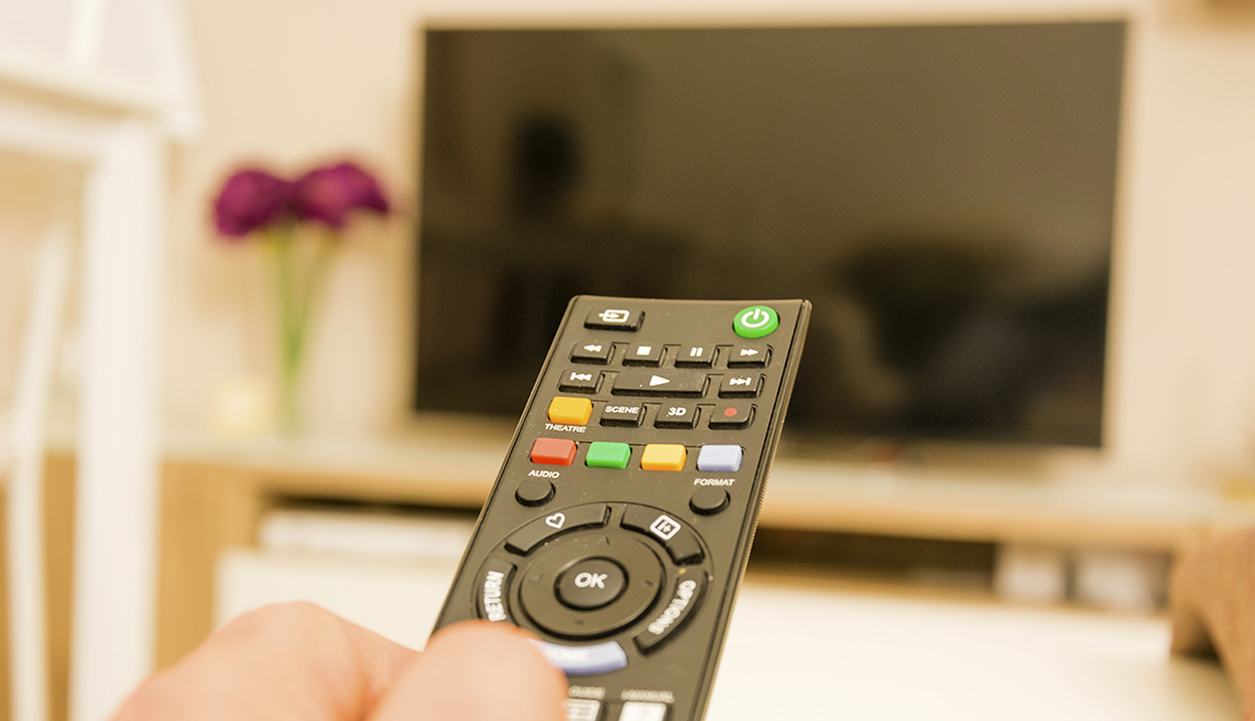 A television remote control being held in a bright room while pointed at a television