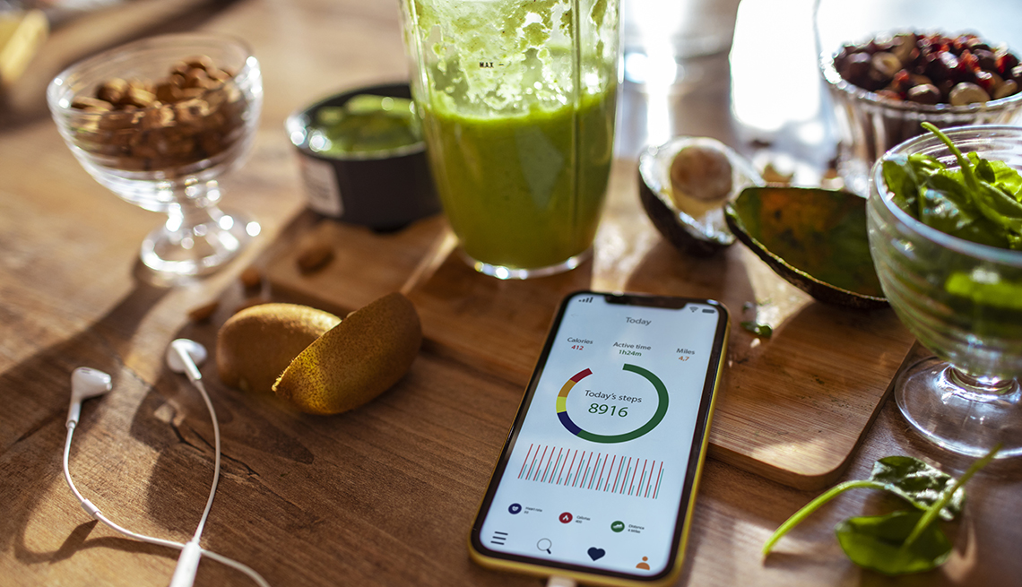 A phone with a step-tracking health app, a juice cleanse drink and healthy food in the background