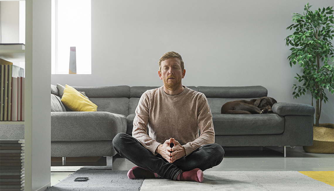 Un hombre medita sentado en el piso de su sala