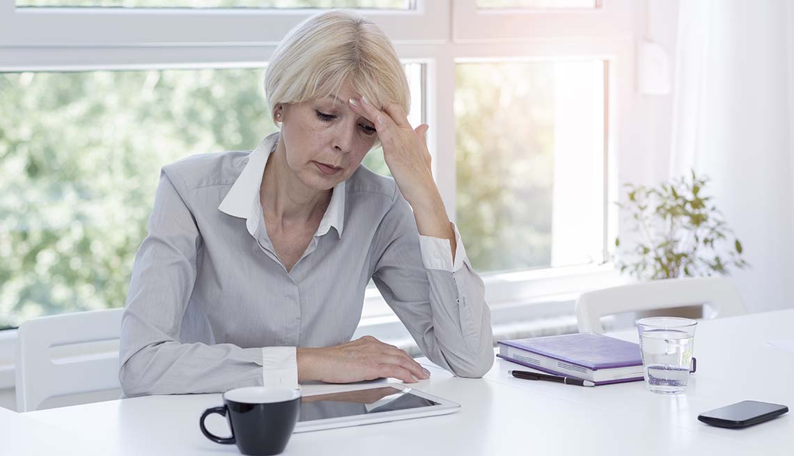 Mature businesswoman with hand on her head sitting at a desk, looking stressed. 