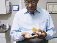 African American mature male sitting on an examination bed in a doctor's office, looking at prescription pills.