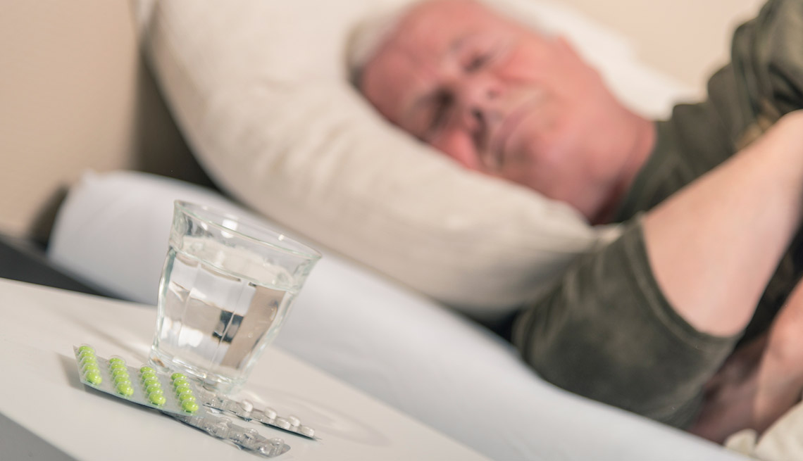 Hombre durmiendo mientras hay un vaso de agua y unas píldoras en una mesa