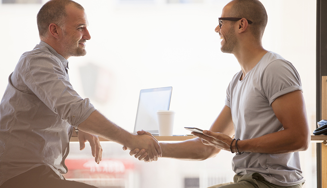Men shaking hands seated at a table, Workplace hearing loss coping strategies