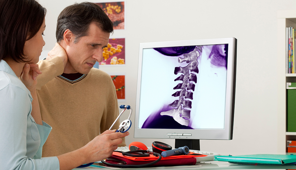 A mature man getting an orthopedics consultation. The computer screen shows an xray of his neck.