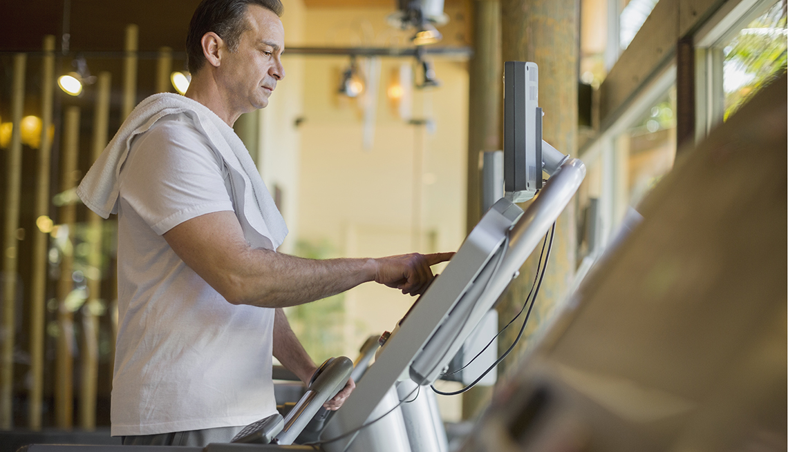 Mature man looking serious, changing the settings on a treadmill.