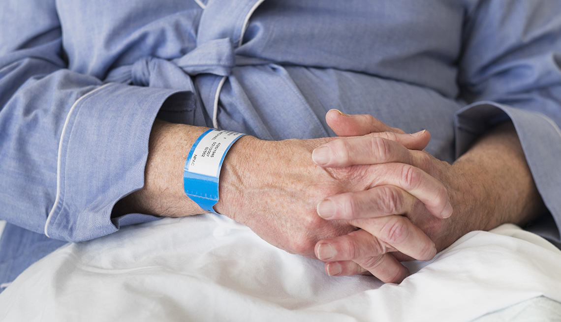 Mature man sitting in hospital bed, wearing a hospital wrist band.