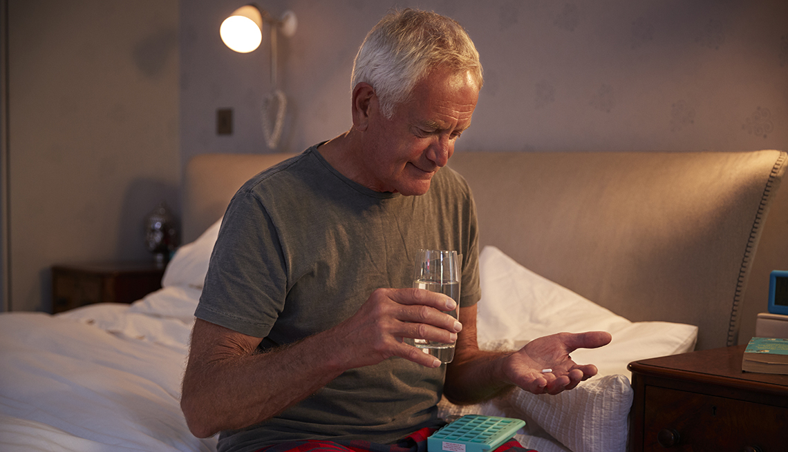 Un hombre toma sus medicamentos sentado en su cama
