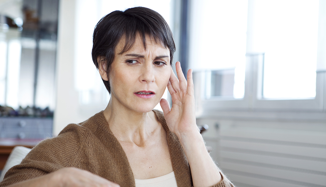 A woman places her fingers near her ear as she suffers discomfort from tinnitus