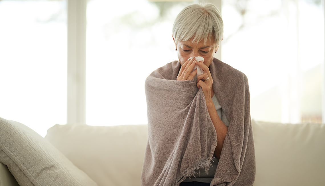 Una mujer con resfriado se limpia la nariz y está arropada con una manta 